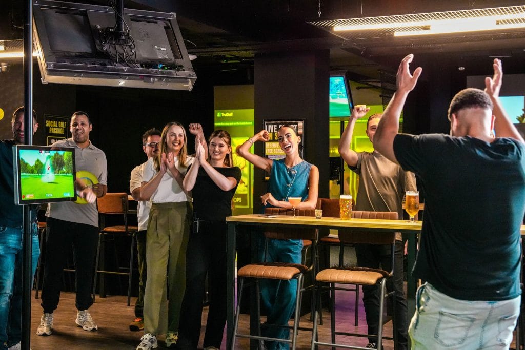 A group of friends cheering while playing the golf simulator at Hukd Golf