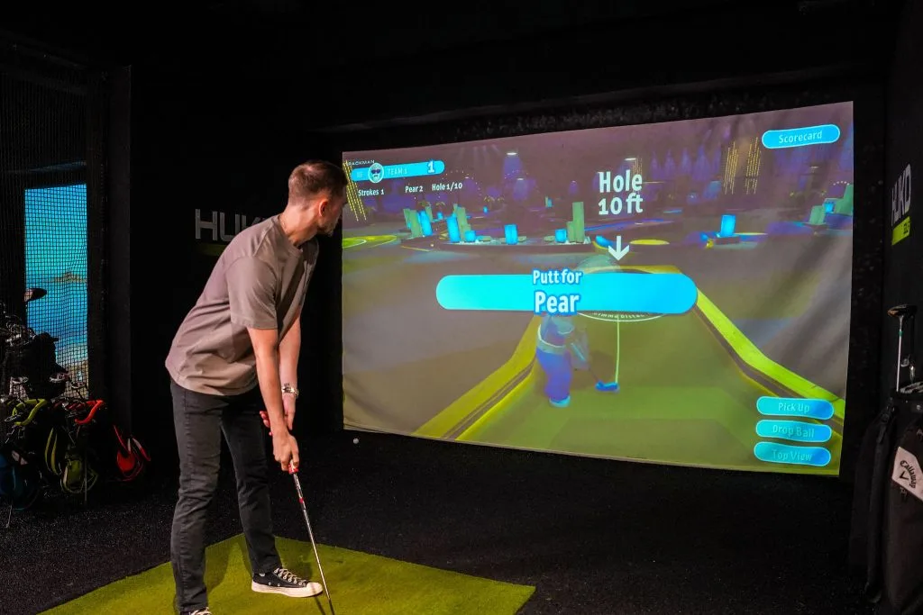 A man playing a mini game on the indoor golf simulator at hukd